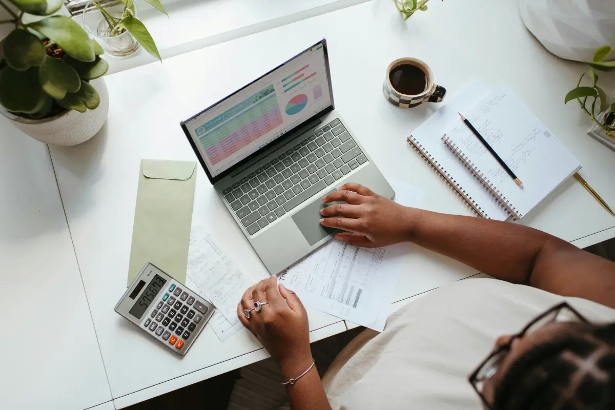 An accountant working on a laptop with a calculator and notepad nearby
